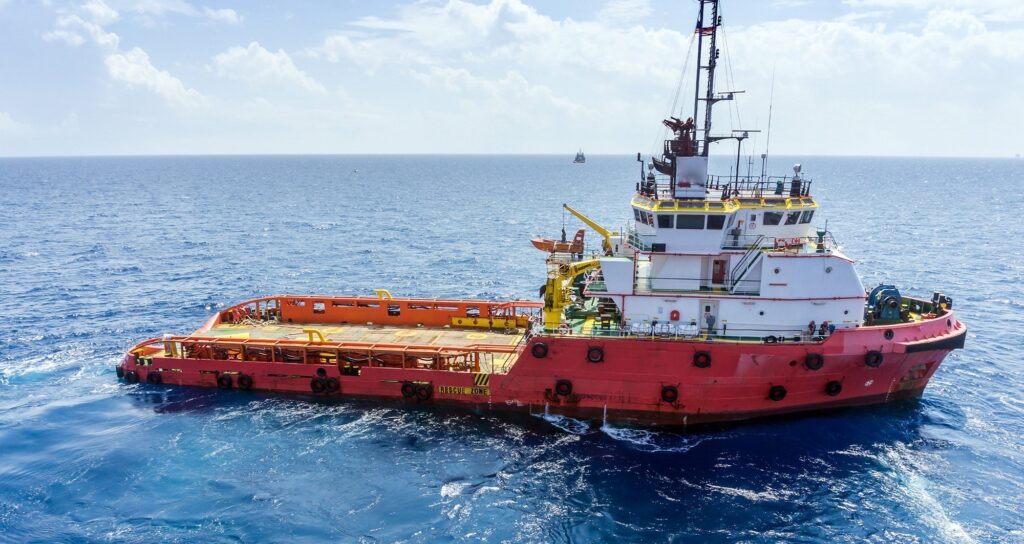 A large red and white marine vessel, an offshore tugboat, with an orange work deck floats on the open ocean under a partly cloudy sky. This type of vessel often relies on powerful diesel engines, such as those remanufactured by SRX Engines, for marine applications.